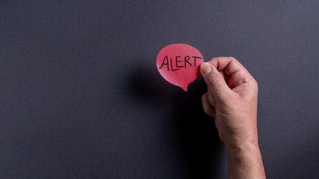 Male hand holding red speech bubble with alert text on dark background