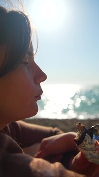 Profile woman eating as a relaxed lady enjoys a tasty wrap while sitting on the beach during a bright sunny day
