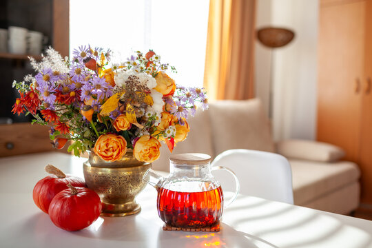 Fall interior decor of living room. Drinking tea at home decorated for autumn with flowers, pumpkins on table. Thanksgiving vibe