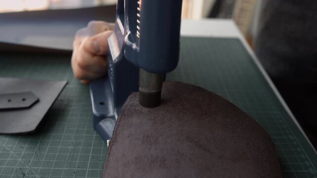 Leather craftsman installing a metal snap button on brown leather using a hand press in a workshop