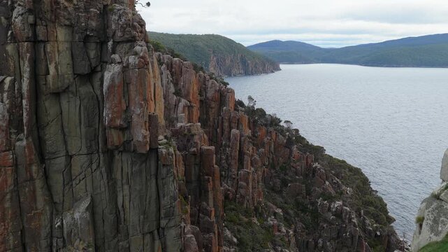 Aerial view of towering columnar rock cliffs beside a broad body of wa