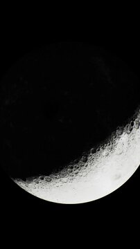 A slender crescent moon hangs in the night sky, casting a soft glow against the deep darkness. Its illuminated edge glistens, highlighting the craters and textures on its surface.