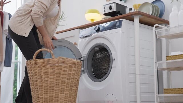 Laundry basket beside washing machine with woman holding clothing in wicker hamper, bright home appliance room for domestic washing chore scene