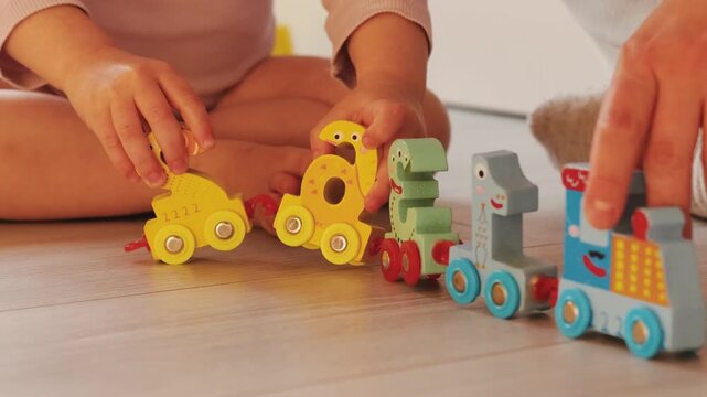Close-up of mother and child hands arranging colorful numbered train pieces together during play.