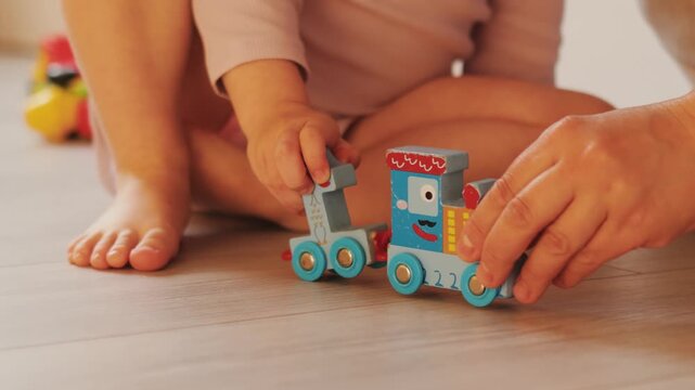 Close-up of child and mother hands playing together with a colorful toy train made of numbers.