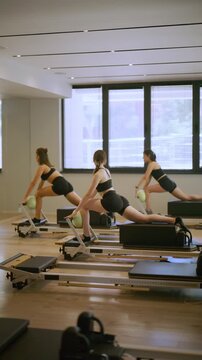 Three women engage in a synchronized Pilates workout on reformer machines. They perform exercises with precision in a bright and spacious fitness studio.