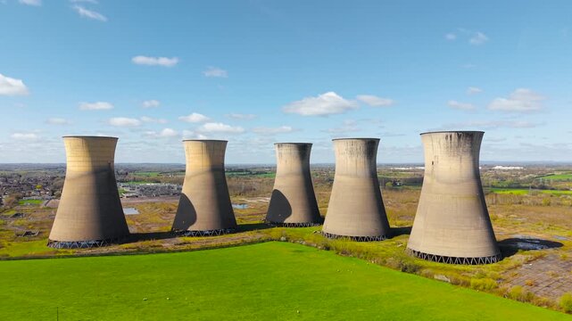 Derelict atomic power plant towers aligned across rural fields post industrial site and ecology transformation theme. Agricultural land contrasting with unused energy complex. Concrete towers forming
