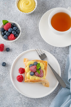 Danish puff pastry cakes with custard cream and fresh berries, sprinkled with powdered sugar on a white plate on a concrete background.