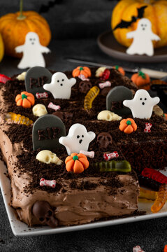 Halloween chocolate cake. Dirty cake with chocolate cream, decorated with worms, skulls, ghosts, pumpkins and sugar sprinkles on a dark background.