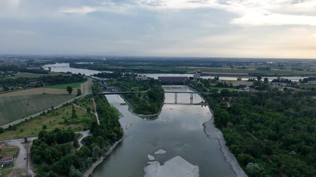 Isola Serafini Dam spans the Po River near Monticelli d'Ongina, Piacenza, during severe summer water scarcity, with exposed river margins and the Adda confluence beyond, aerial.
