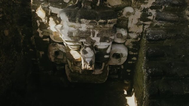 Detailed close-up shot reveals the intricately carved Mask of Chaac, Maya rain god, on weathered stone at Tikal, bathed in natural sunlight and shadow, showcasing ancient craftsmanship.