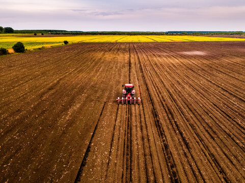 Tractor with planter seeding a large brown farm field, preparing for crop growth with yellow fields in background