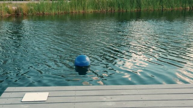 Blue buoy floats near a dock as lake water moves from left to right.