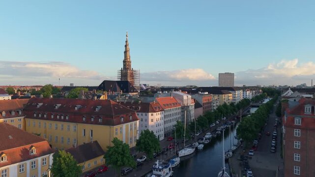 Drone footage ascending above the Christiania canal, unveiling Copenhagen's urban landscape with the iconic spiral belfry of Our Saviour's Church (Vor Frelsers Kirke) in the background.