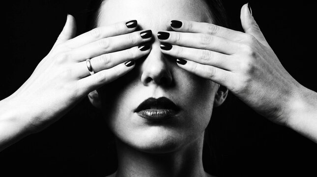 Dramatic black and white portrait of woman covering eyes with hands
