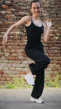 Young professional Hispanic dancer performing salsa in front of a brick wall while recording a video for social media, capturing urban dance culture, energy and modern content creation.