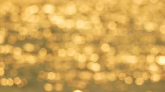 Liquid amber sunlight dances on rhythmic sea surface ripples during a quiet afternoon by the coast. Rack focus pull cinematic shot.