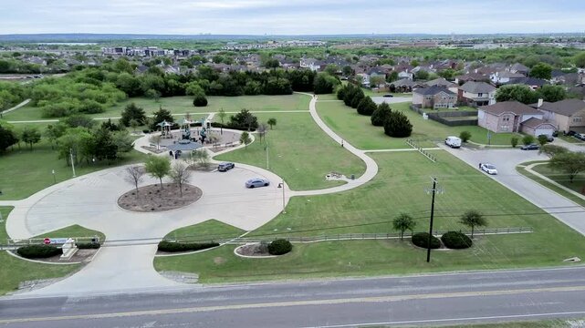 Paved walking circuit circles playground amenities at Eden Road Park along Mansfield Webb Road. Open grass fields, parked vehicles, roadside power cables show public recreation, Arlington, Texas