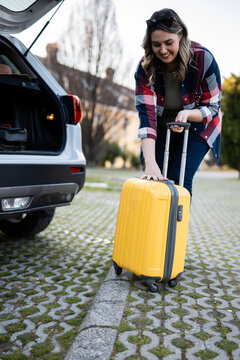 Woman loading yellow suitcase into car for travel