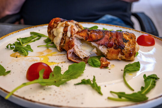 Pork roulade with cheese, plate with herb leaf, oil and cherry tomato.
