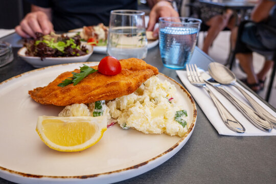 Pork schnitzel with potato salad and lemon on plate, cutlery, beverage, man.