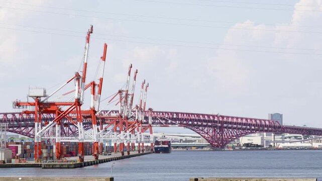 大阪南港のコンテナターミナルに並ぶ大型のガントリークレーンとトラス構造の赤く大きい港大橋港大橋