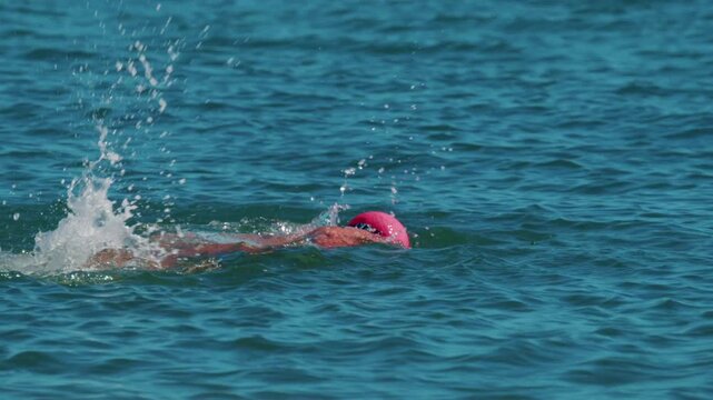 Professional swimmer performs freestyle stroke in deep blue ocean water.