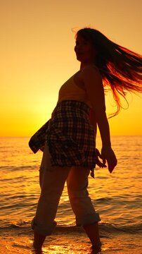 Golden hour energy portrays a female dancer flowing gracefully with long hair against a marine backdrop. Static vertical medium shot.