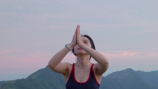 Young woman practicing yoga and meditation with hands raised in prayer pose during sunset at Mau Son mountains, Vietnam. Wellness, mindfulness, and outdoor fitness lifestyle concept