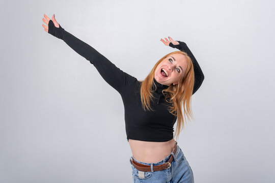 Red haired woman laughing with arms raised in a celebratory pose, radiating joyful energy, triumph and carefree happiness against a clean white studio background