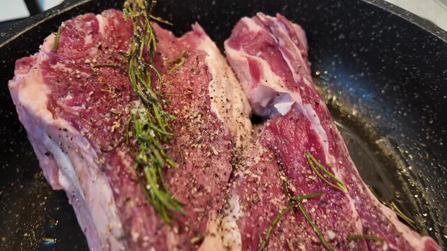 Raw lamb chops seasoned with rosemary salt and pepper cooking in a pan.