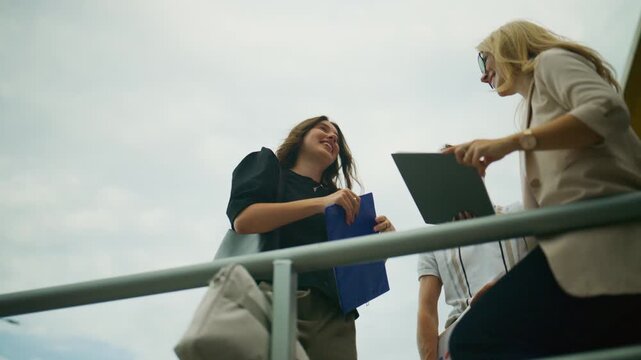 Three business people are seen collaborating and discussing documents outdoors. Professional colleagues review important reports and share ideas in a bright, open setting.