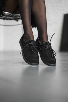 Closeup of crossed female legs wearing sheer black stockings and suede laceup shoes in modern interior, with stocking, hosiery, legs, female detail, showing woman, sheer, black, nylon context