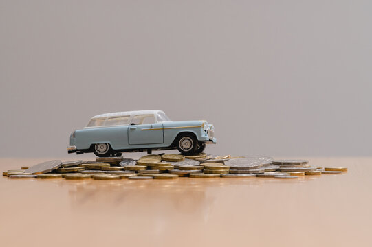 blue historic toy car drive over pill of coins in concept of car insurance financial status for buying a new car, car leasing, down payment and instalments in the long term.