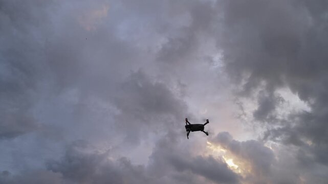 Low angle view of drone entering frame and hovering against clouds