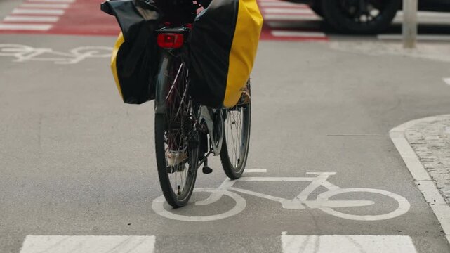 Cyclist riding along designated urban bike lane with prominent bicycle road markings and red pavement at crossing, modern cycling infrastructure, active mobility and sustainable transportation