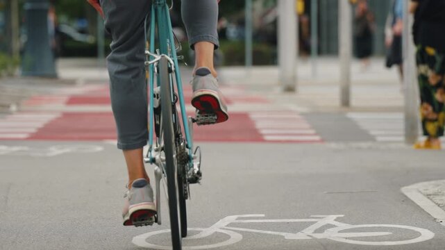 Close-up slow motion cyclist riding designated urban bike lane with prominent bicycle road markings and red pavement at crossing, modern cycling infrastructure, active mobility and transportation