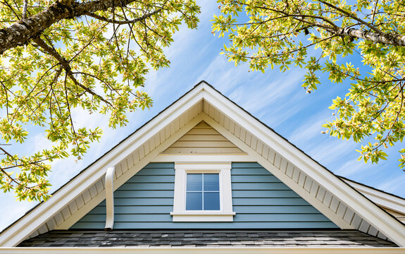 Residential house gable roof with white gutters and siding under blue sky