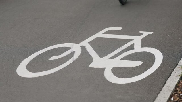 Cyclist riding along designated bike lane in modern city, close-up view of bicycle crossing white bicycle lane markings and road symbols, urban cycling infrastructure and sustainable transportation