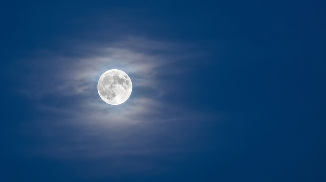 Bright full moon illuminated amidst wispy clouds against a deep blue night sky, a celestial spectacle