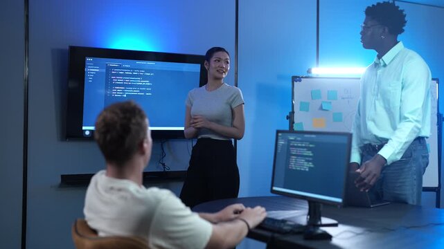 Diverse IT teams collaborating in modern offices. Asian female software developer presenting code on large screen to male programmers. Corporate technology, coding review and business teamwork