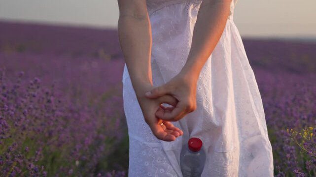 Woman dancing fingers play rhythmically in front of a plastic bottle within a sunset lavender field. Static close-up shot.