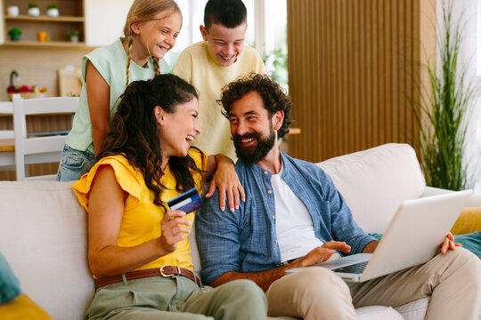 Happy family together on the sofa at home, parents and children enjoying online shopping with a credit card and laptop, experiencing modern digital convenience and e-commerce