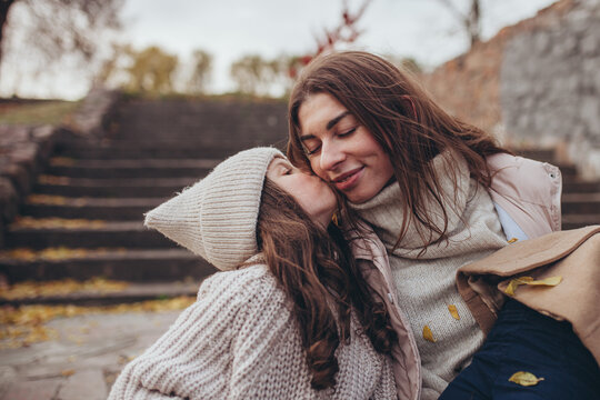 Tender moment of young girl kissing her mother on cheek during autumn walk outdoors. Unconditional love, warmth, family happiness, childhood, togetherness, emotions of care, affection.