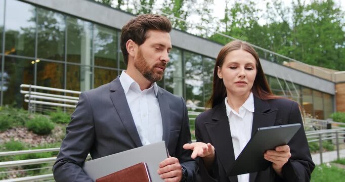 Business man and woman discussing project on digital tablet outdoors