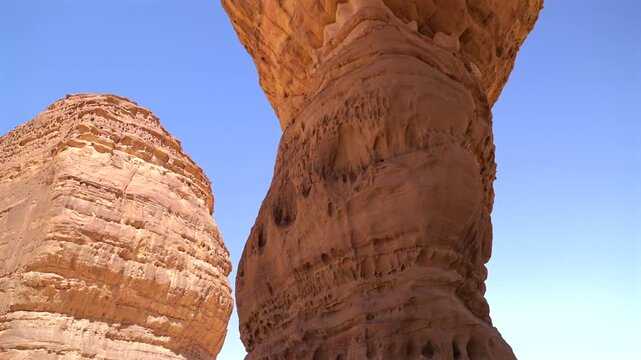 Cinematic close-up of unique wind carved sandstone rock formation resembling Elephant Rock arch in AlUla desert