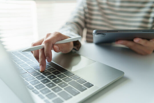 Creative professional uses a stylus with a digital tablet and laptop at home, representing digital design, creative workflow, drawing, editing, freelance work and modern productivity.