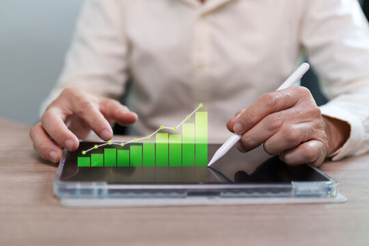 Businessman uses a stylus on a digital tablet with a rising green chart, representing energy efficiency, renewable technology, sustainable growth, cost savings and environmental business strategy.