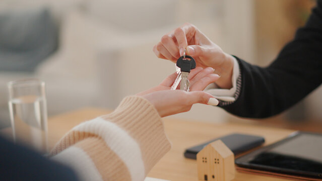 Property agent hands house keys to a buyer beside a model home and documents, representing real estate purchase, home ownership, mortgage approval, property investment and successful sale.