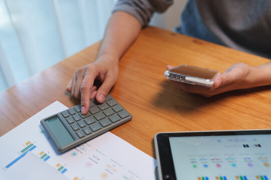 Professional reviewing financial documents with a calculator, smartphone, and tablet for budgeting, expense analysis, and business planning.